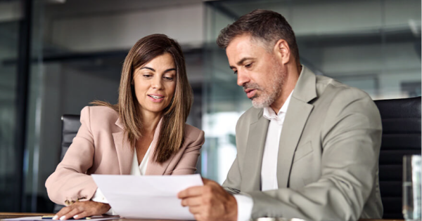 A woman and man in business outfits sitting down and going over a paper document together