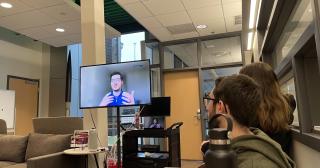 Guest speaker on a monitor speaking with students in a lounge area