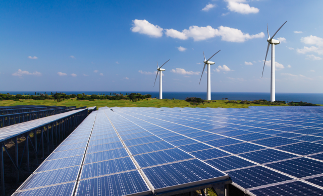 A set of solar panels with windmills in the background on a sunny day.