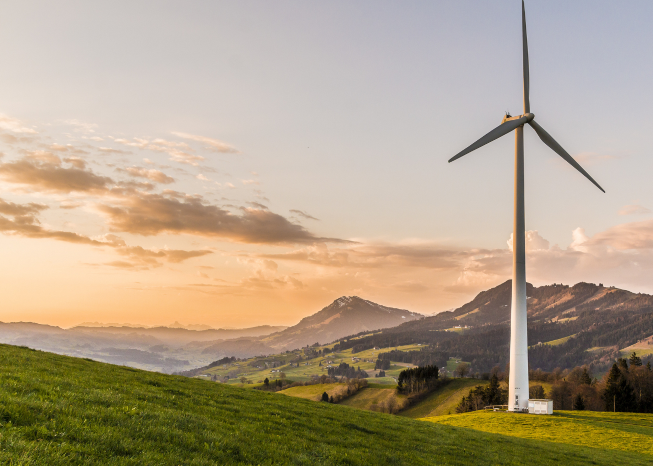 A windmill on a grassy area with a sunset behind the mountains