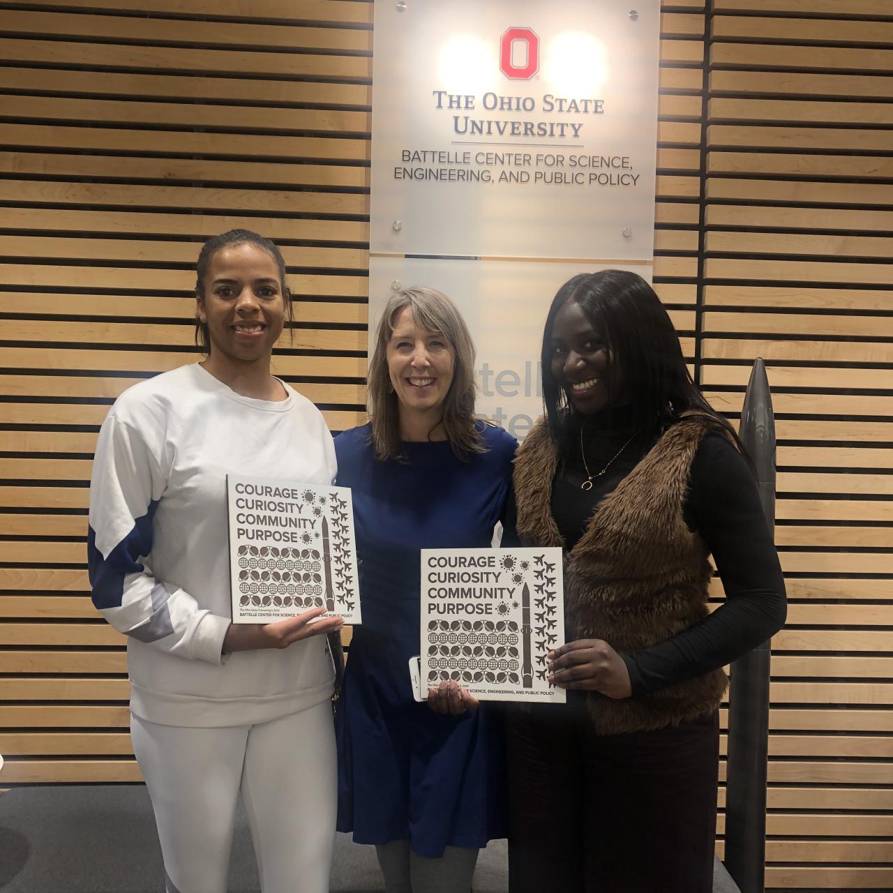 Dr. Newton surrounded by two alumni holding their 2019 graduation plates
