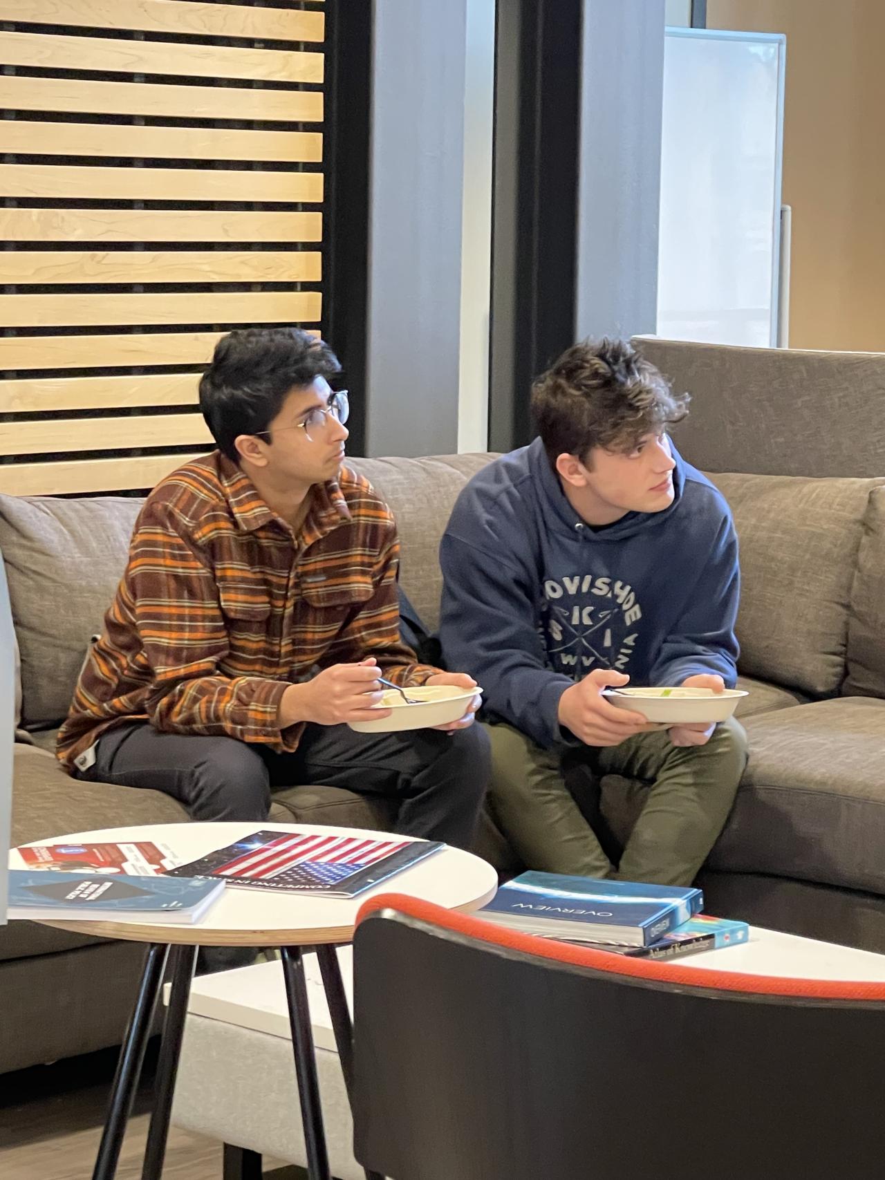Two students sitting on a couch listening to someone out of the picture.