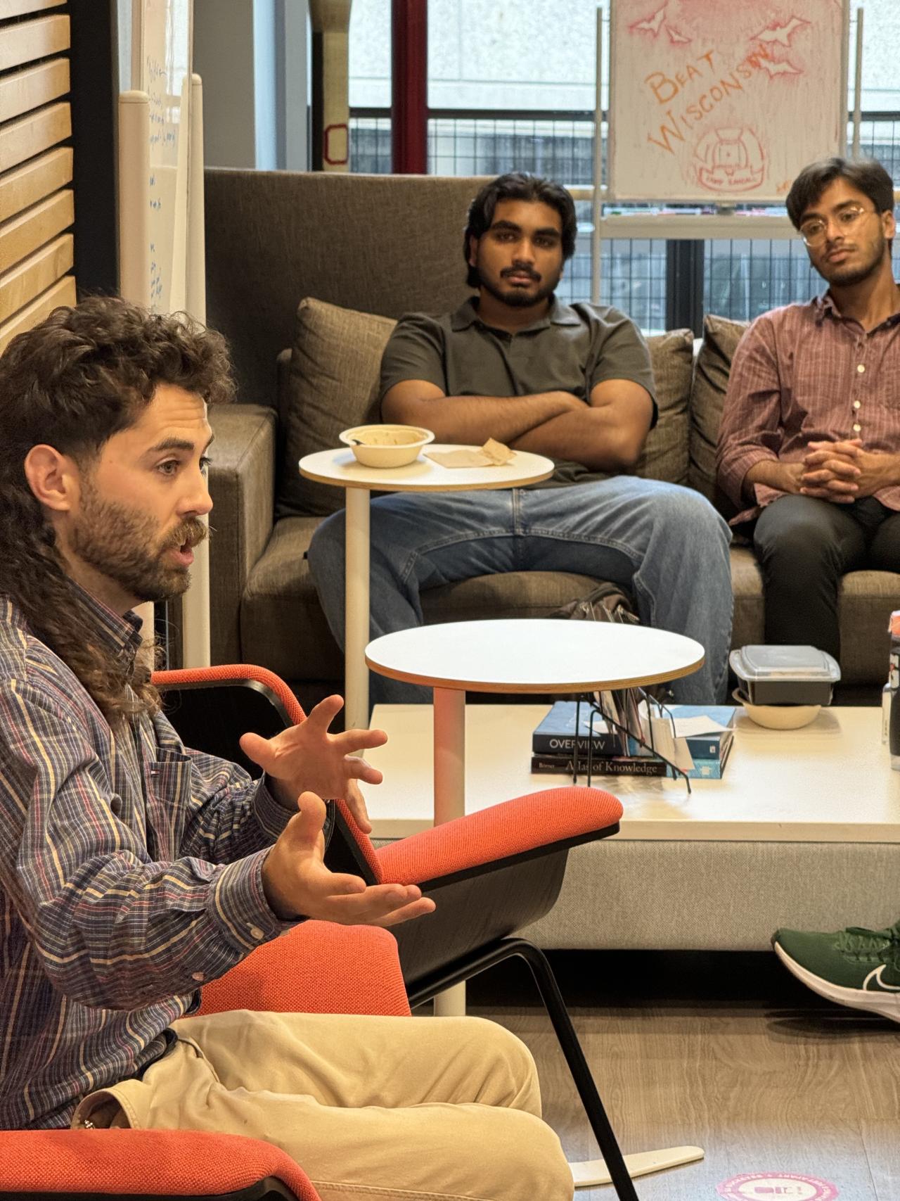 Speaker on the left with two people in the background on a couch listening