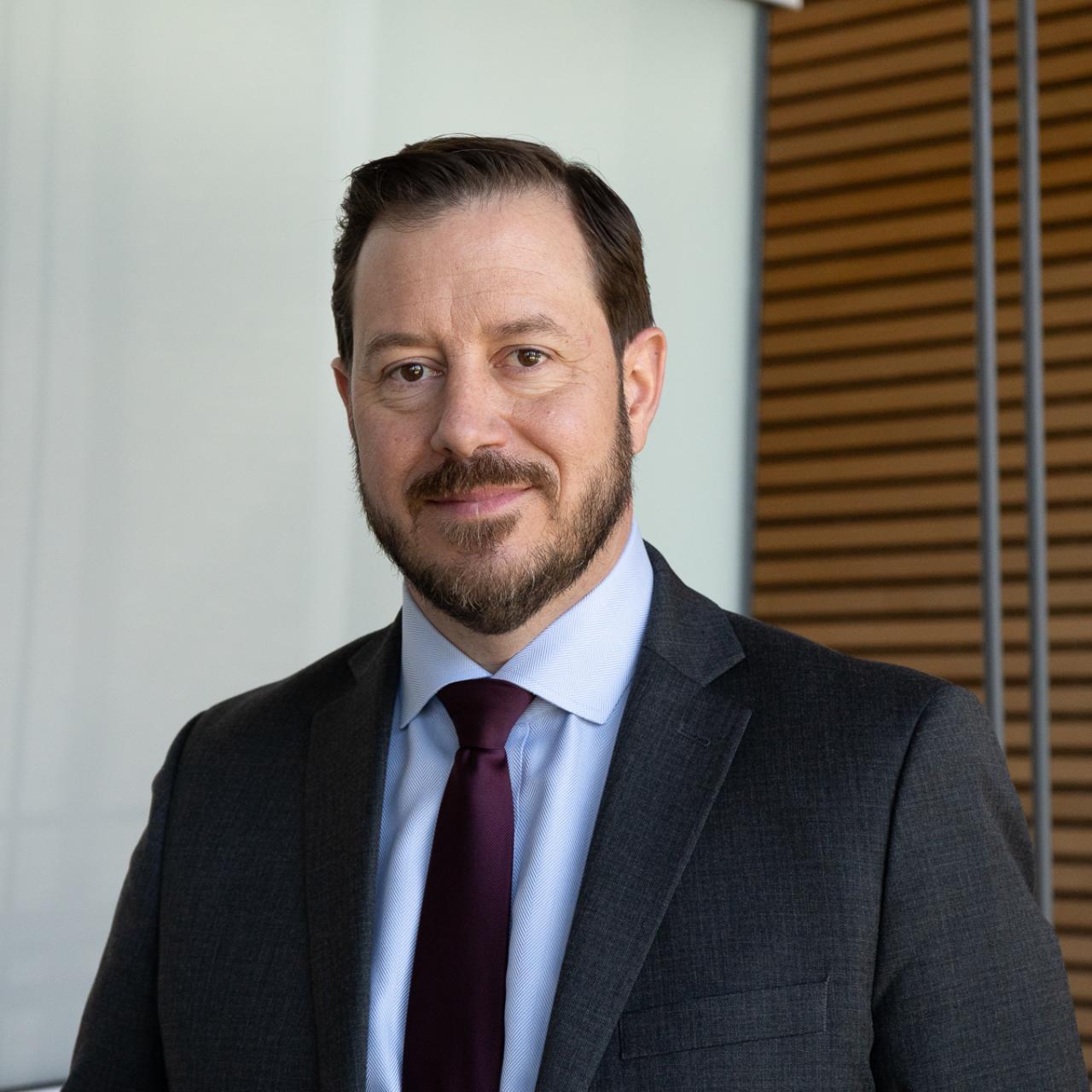 Headshot for of Dan Kelley in a suit with a glass and wood background