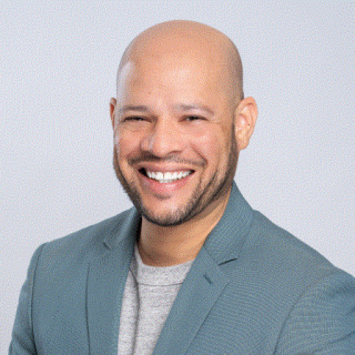 A headshot of Michael Pires in a dark blue-gray suit against a light gray background