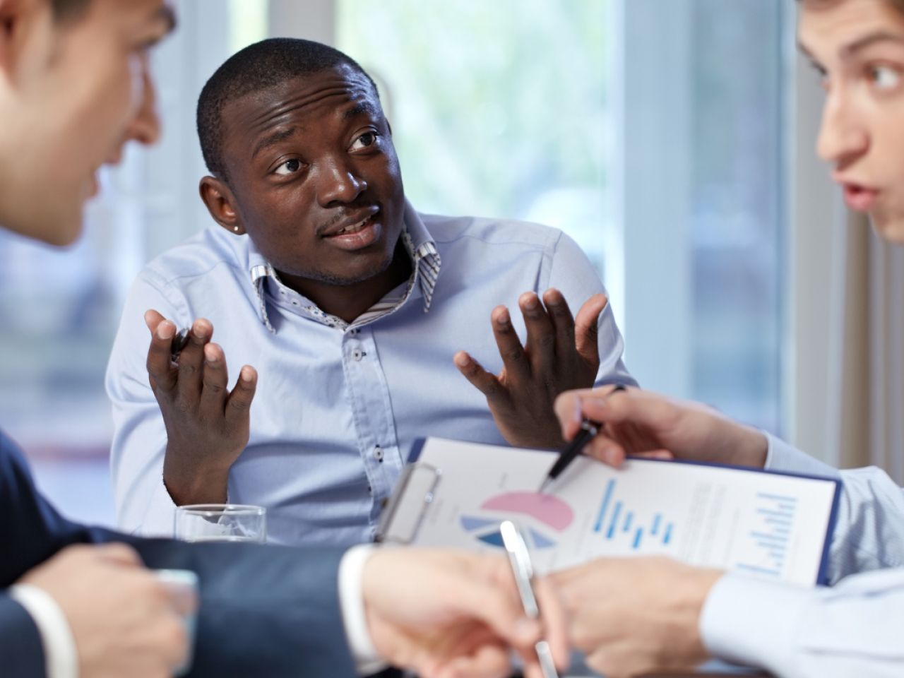 Three men, two on the outside  having a heated conversation over a paper, and the third in the middle with his hands up attempting to mediate