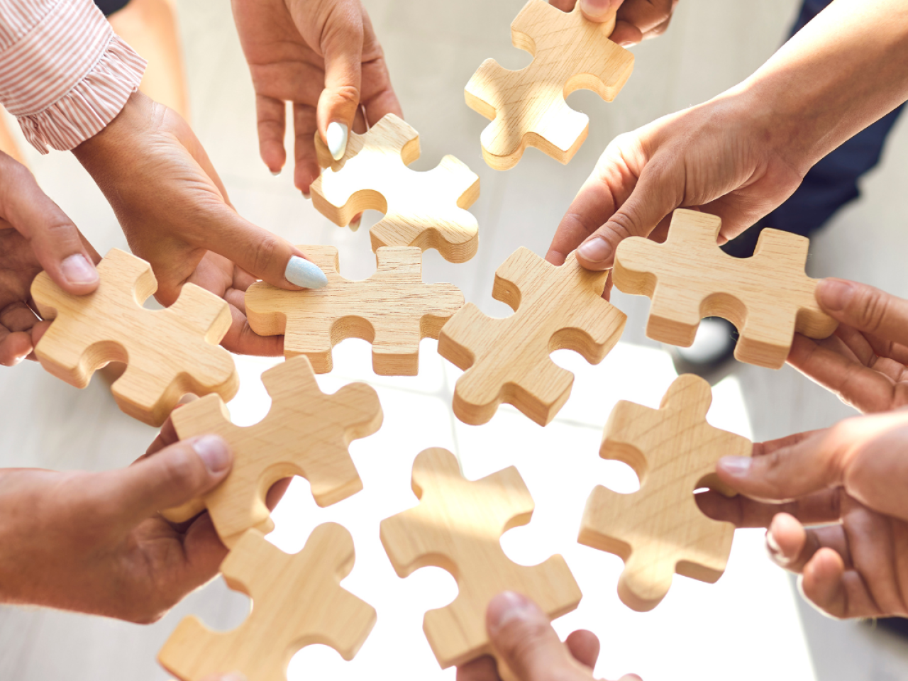 Ten hands of different people holding puzzle pieces into the center of a circle