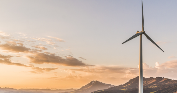 A windmill on a grassy area with a sunset behind the mountains