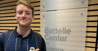 Chase Lyon holding a small astronaut with the Battelle Center Logo in the background