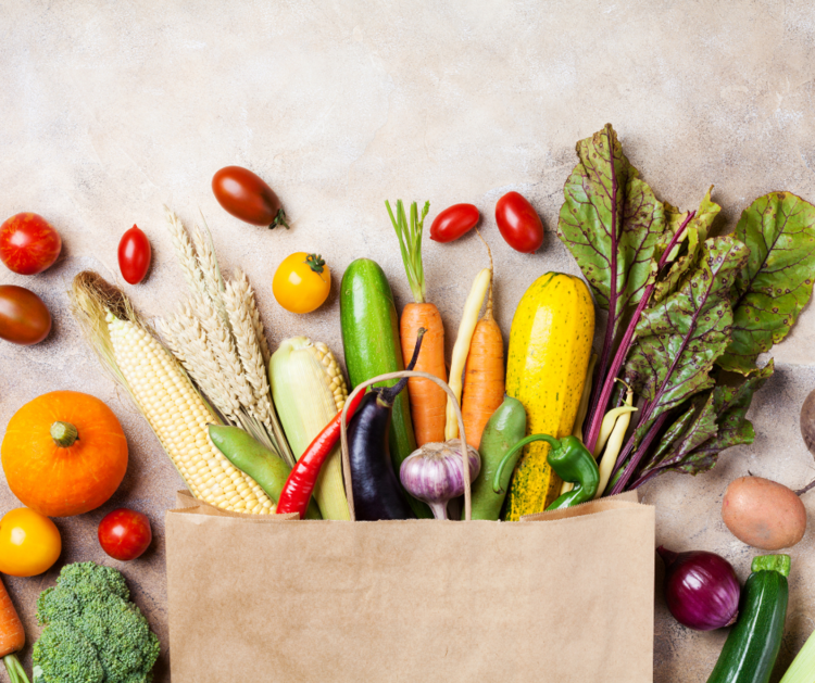 An assortment of vegetables and fruits spread on a table from a paper grocery bag