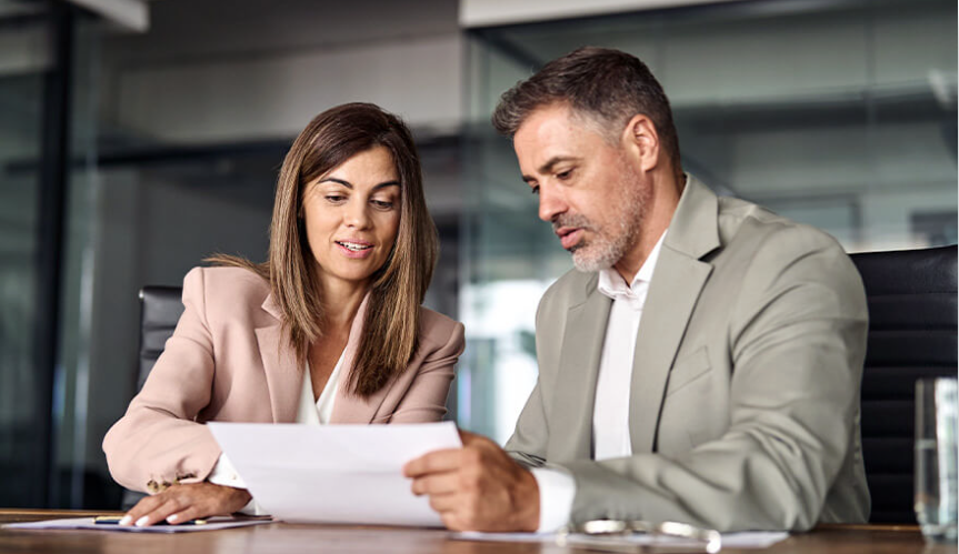 A woman and man in business outfits sitting down and going over a paper document together