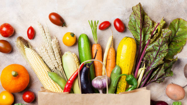 An assortment of vegetables and fruits spread on a table from a paper grocery bag