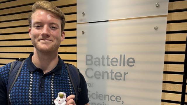 Chase Lyon holding a small astronaut with the Battelle Center Logo in the background