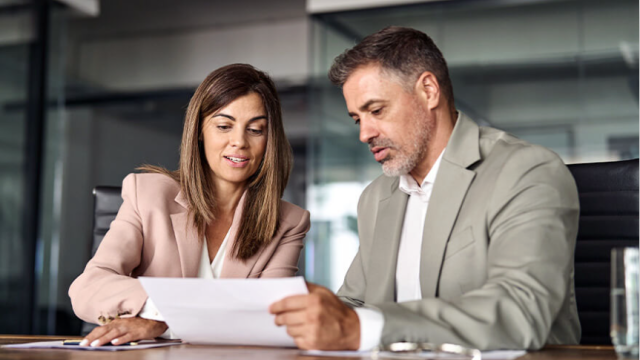 A woman and man in business outfits sitting down and going over a paper document together